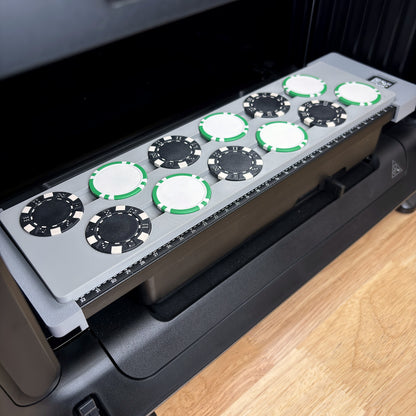 Samcraft poker chip jig on the bed of a eufyMake E1 UV printer, loaded with 12 poker chips in two staggered rows, black dice-stripe chips alternating with white chips edged in green stripes.