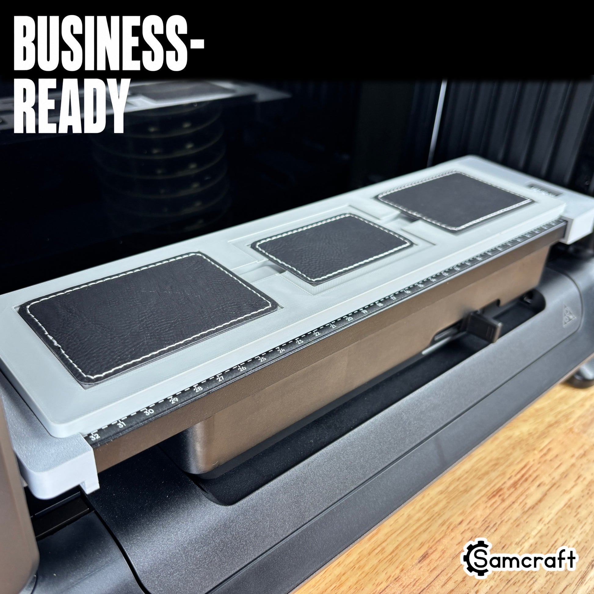 Rectangle Patch Jig for the eufyMake E1 — angled view of the gray 3D-printed tray holding three black stitched leather rectangle patches on the printer bed with built-in alignment ruler, highlighting the business-ready design.