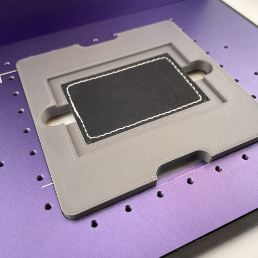 Samcraft rectangle patch jig on the purple bed of a WeCreat Lumos, holding a rectangular black leatherette patch.