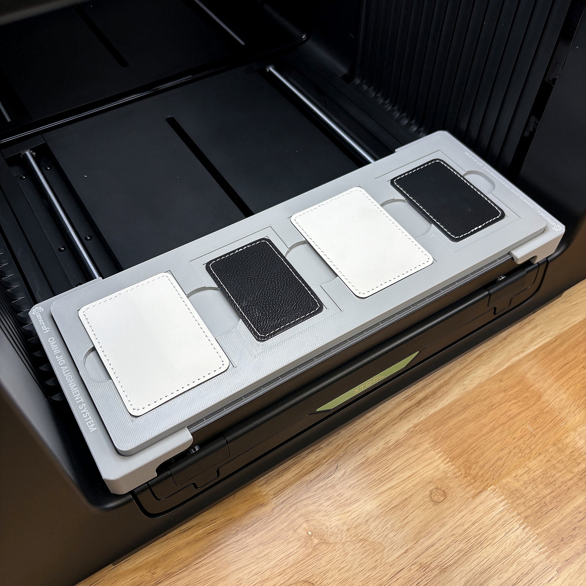 Samcraft rectangle patch jig on the bed of an xTool Omni UV printer, loaded with four leatherette patches.