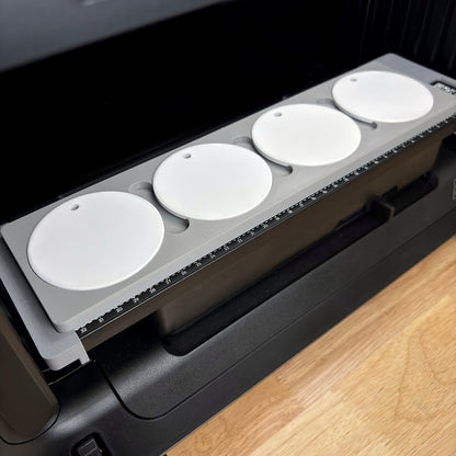 Samcraft round ceramic ornament jig on the bed of a eufyMake E1 UV printer, holding four white round ceramic ornaments in a row beside the bed's built-in ruler.
