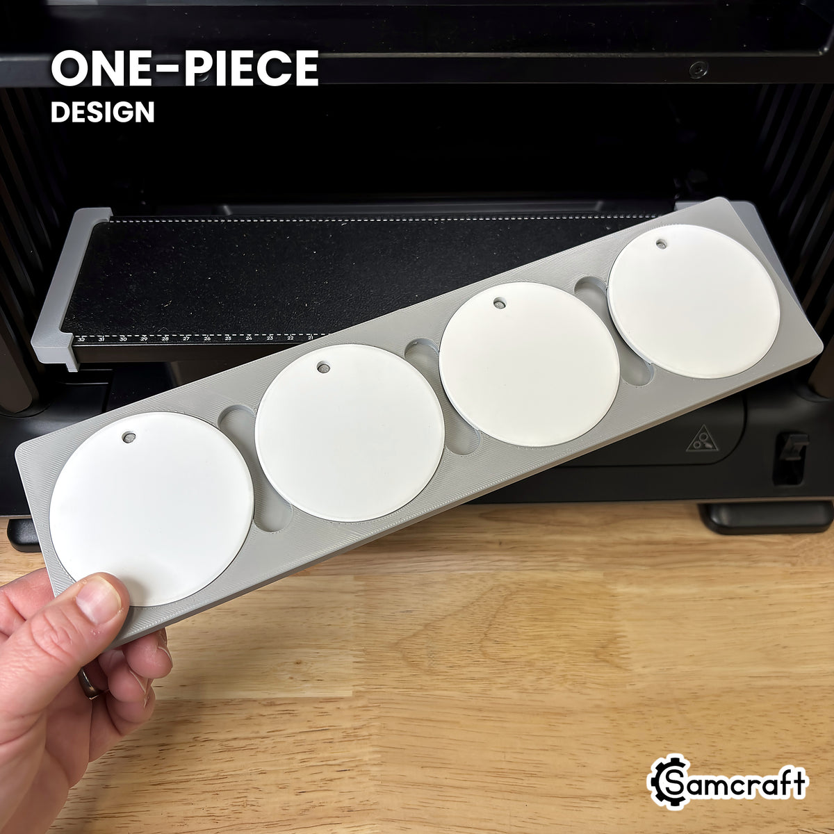 Hand holding the one-piece Samcraft round ceramic ornament jig for the eufyMake E1, four white ceramic ornaments seated in a single molded gray tray.