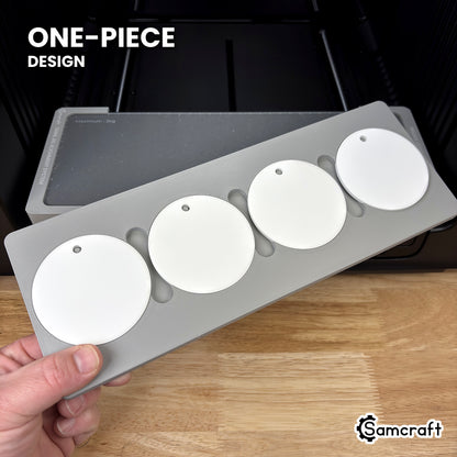 Hand holding the one-piece Samcraft round ceramic ornament jig for the xTool Omni, four white ceramic ornaments seated in a single molded gray tray.