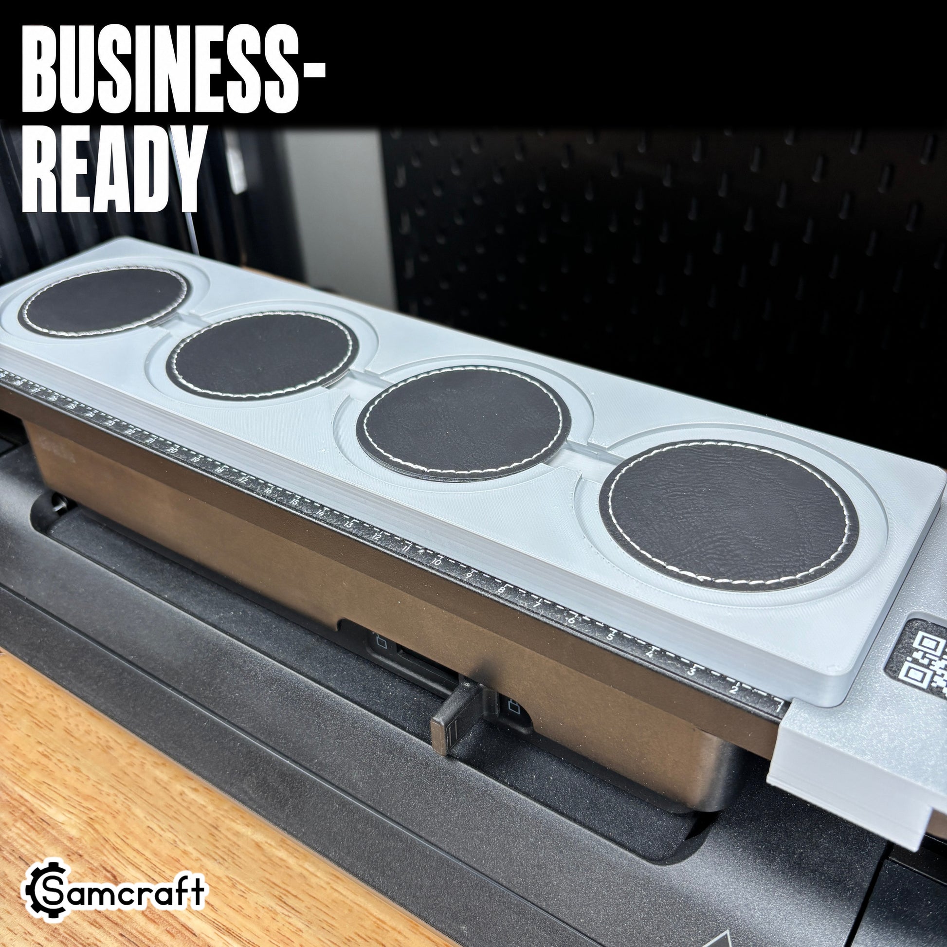 Round Patch Jig for the eufyMake E1 — four round black leather patches with white stitched borders seated in the gray 3D-printed tray with built-in alignment ruler and QR code, ready for business-scale personalization.