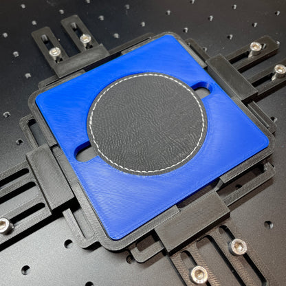 Samcraft blue round patch jig on a ComMarker laser bed, holding a round dark leatherette patch.
