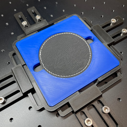 Samcraft blue round patch jig on a ComMarker laser bed, holding a round dark leatherette patch.