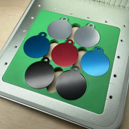 Samcraft round pet tag jig in an xTool F1 laser bed, holding seven round aluminium pet tags in grey, blue, red and black.
