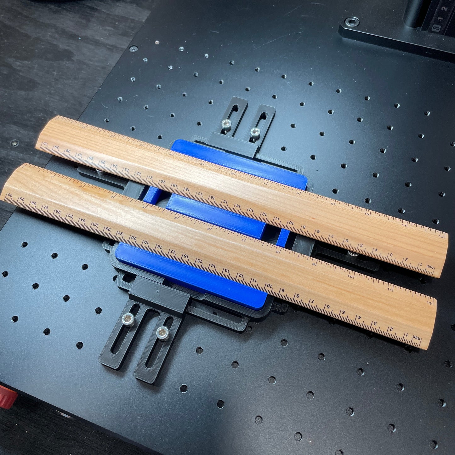 Samcraft blue ruler jig on a ComMarker laser bed, holding two wooden rulers.