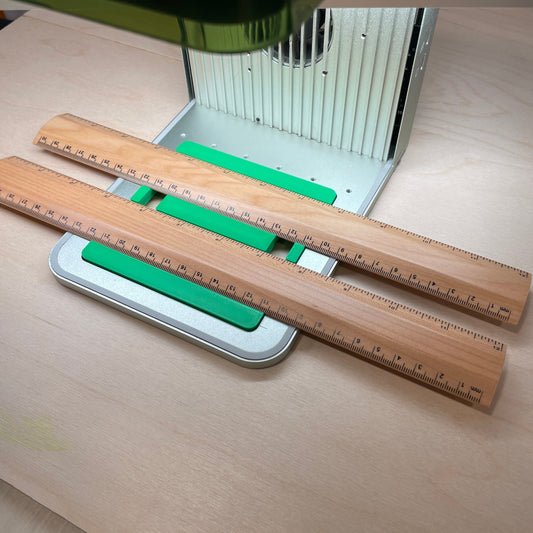 Samcraft green ruler jig in an xTool F1 laser bed, holding two wooden rulers end to end.