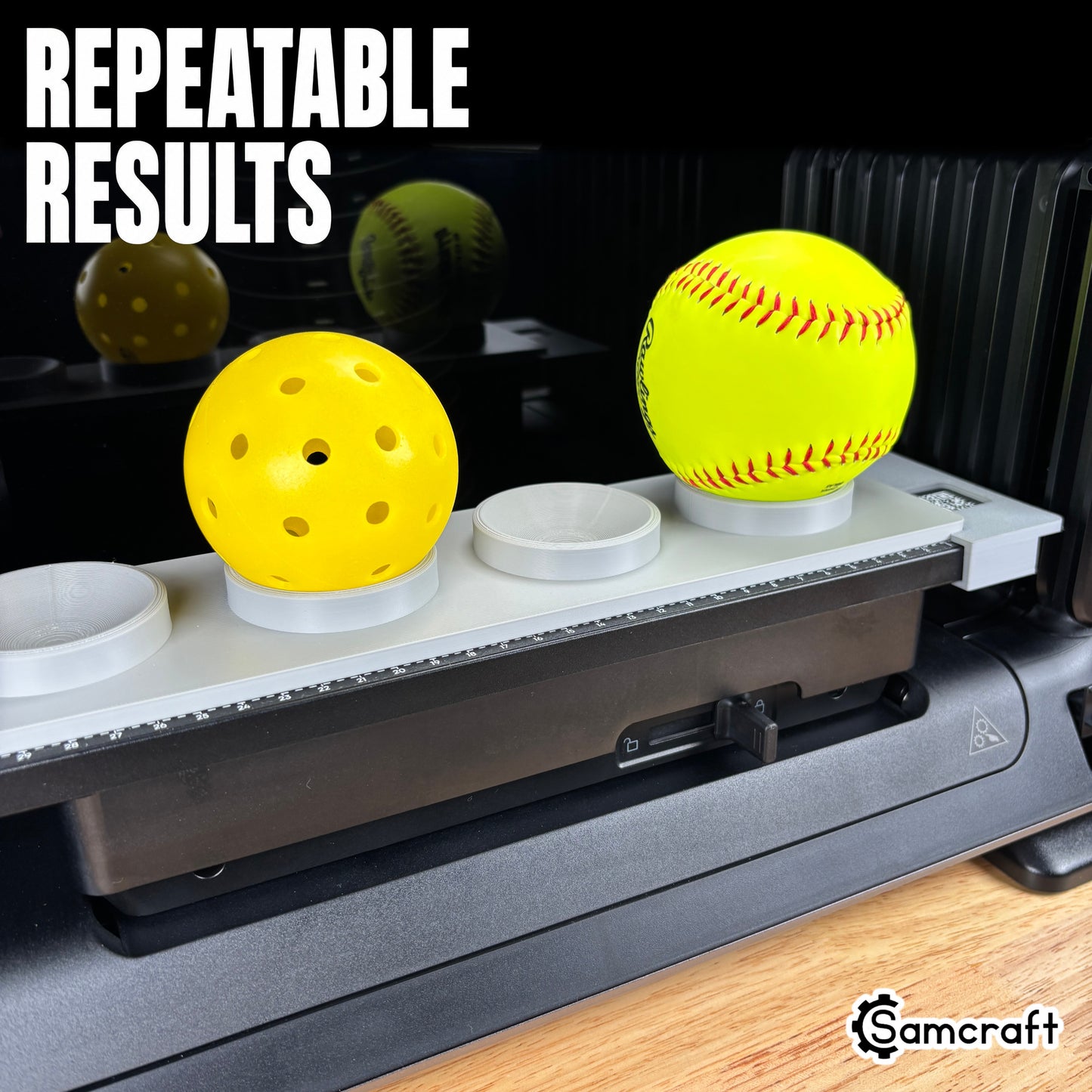 Sports Ball Jig for the eufyMake E1 — gray 3D-printed tray with a pickleball and softball seated in ring holders on the printer bed with built-in alignment ruler, highlighting repeatable results.