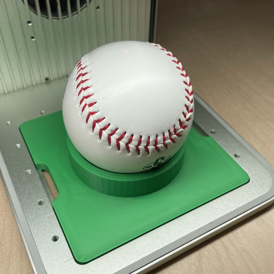 Samcraft green sports ball jig in an xTool F1 laser bed, cradling a baseball in the centre recess.