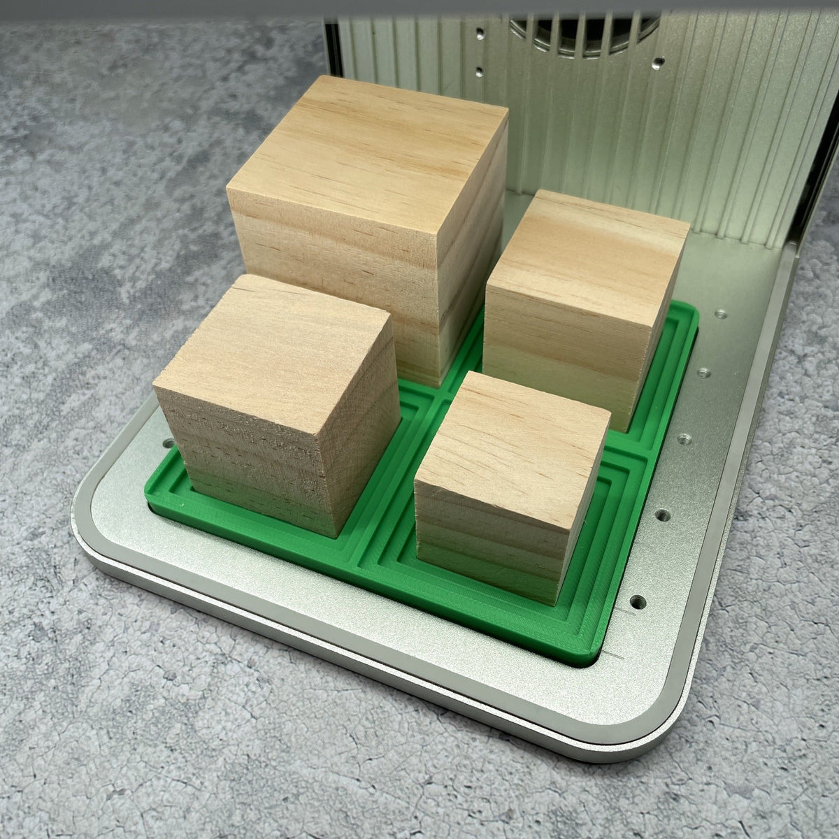 Samcraft medium square block jig in an xTool F1 laser bed, cradling four wooden blocks of different sizes.