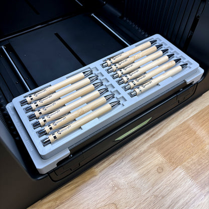 Samcraft universal 12 pen jig on the bed of an xTool Omni UV printer, loaded with twelve bamboo pens.