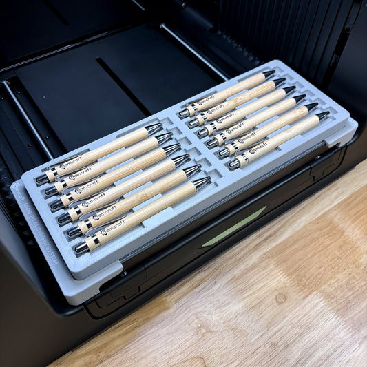Samcraft universal 12 pen jig on the bed of an xTool Omni UV printer, loaded with twelve bamboo pens.