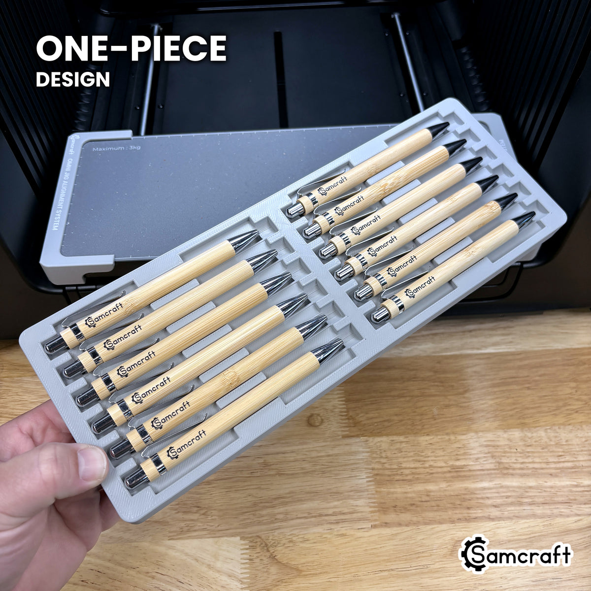 Hand holding the one-piece Samcraft 12 pen jig for the xTool Omni, twelve cradles in a single molded tray.