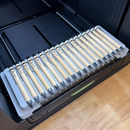 Samcraft universal 18 pen jig on the bed of an xTool Omni UV printer, holding eighteen bamboo pens in curved barrel cradles.