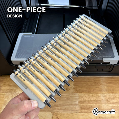 Hand holding the one-piece Samcraft universal 18 pen jig for the xTool Omni, eighteen bamboo pens seated in a single molded gray tray.