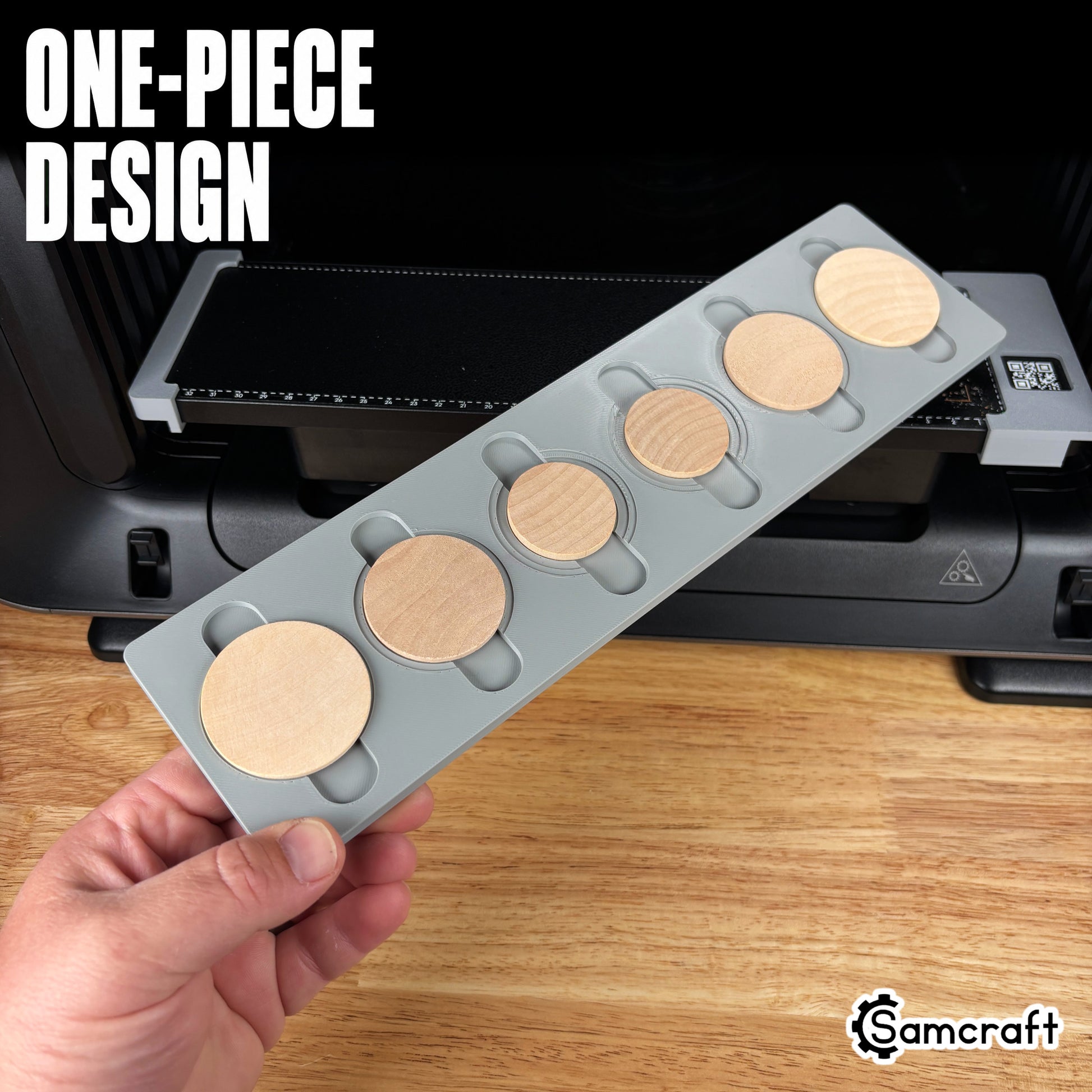 Wood Coin Jig for the eufyMake E1 — hand holding the gray one-piece 3D-printed tray loaded with six round wooden coins of varying sizes, template files included, highlighting the one-piece design.