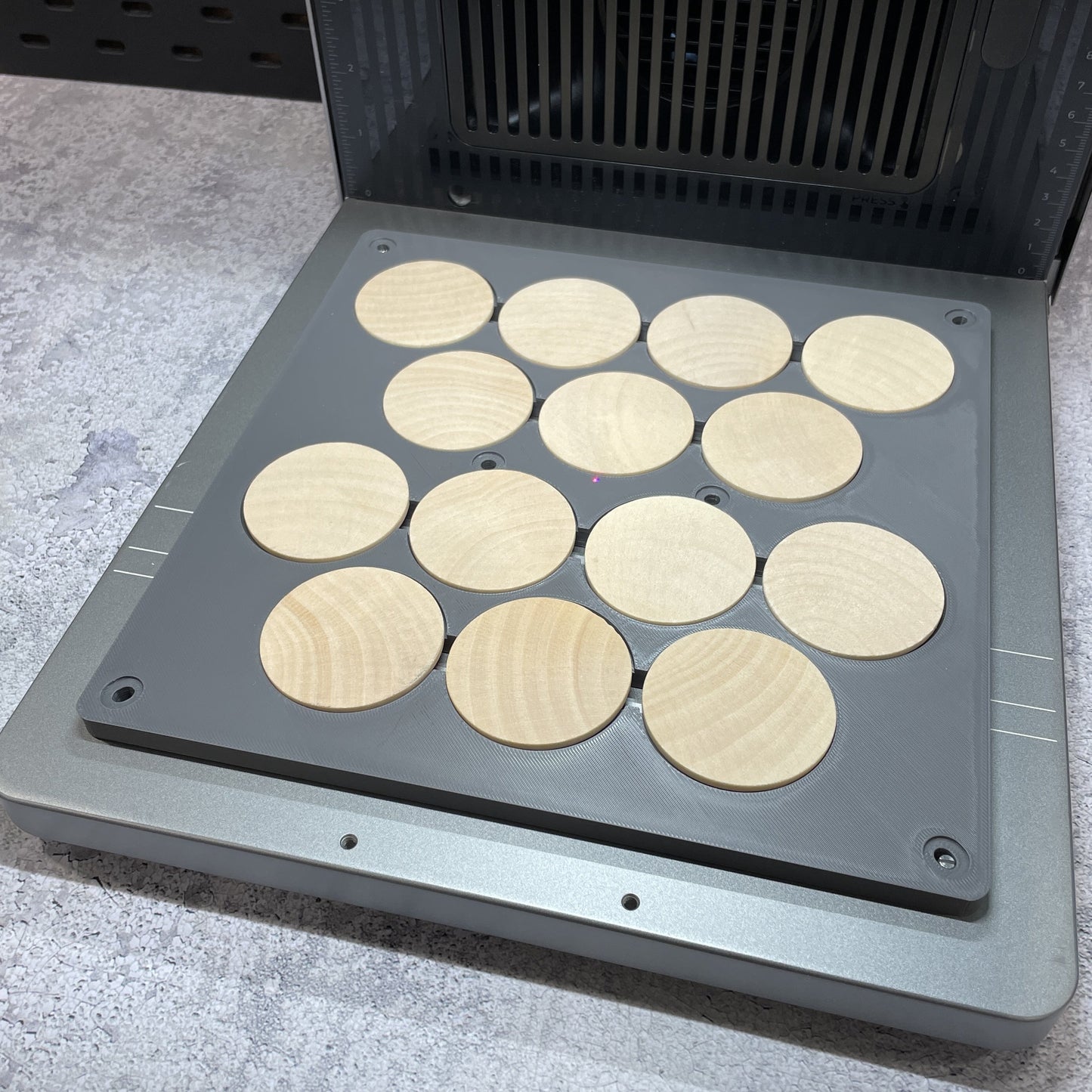 Samcraft wood coin jig on the xTool F2 Ultra bed, holding a full set of round wooden coins.