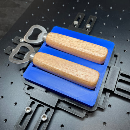 Samcraft blue wood handle bottle opener jig on a ComMarker laser bed, holding two wood-handle bottle openers.