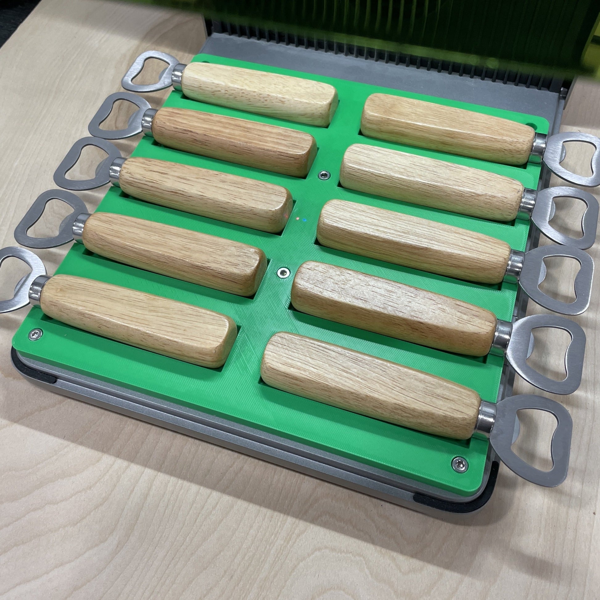 Samcraft green wood handle bottle opener jig in an xTool F1 Ultra laser bed, holding ten wood-handled bottle openers.