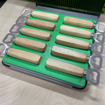 Samcraft green wood handle bottle opener jig in an xTool F1 Ultra laser bed, holding ten wood-handled bottle openers.