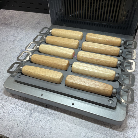 Samcraft wood handle bottle opener jig on the xTool F2 Ultra bed, holding wood-handle bottle openers in channelled slots.
