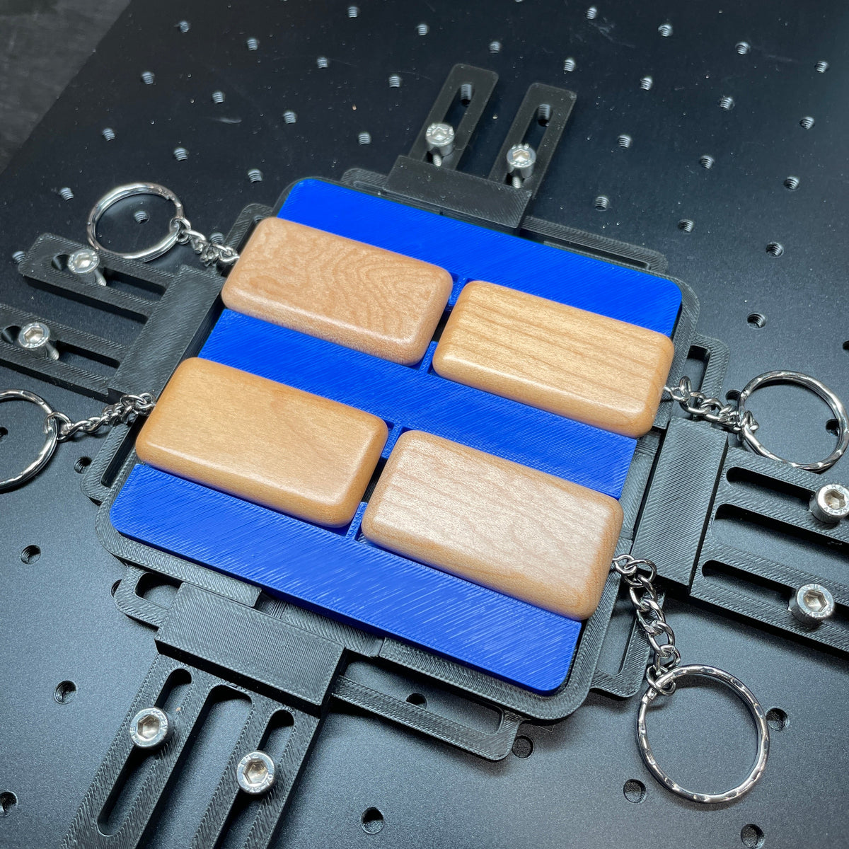 Samcraft blue wood rectangle keychain jig on a ComMarker laser bed, holding wooden rectangle keychains on split rings.